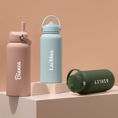Three insulated water bottles with straws, in pink, blue, and green colors, each with different handles and personalized engravings on the front.