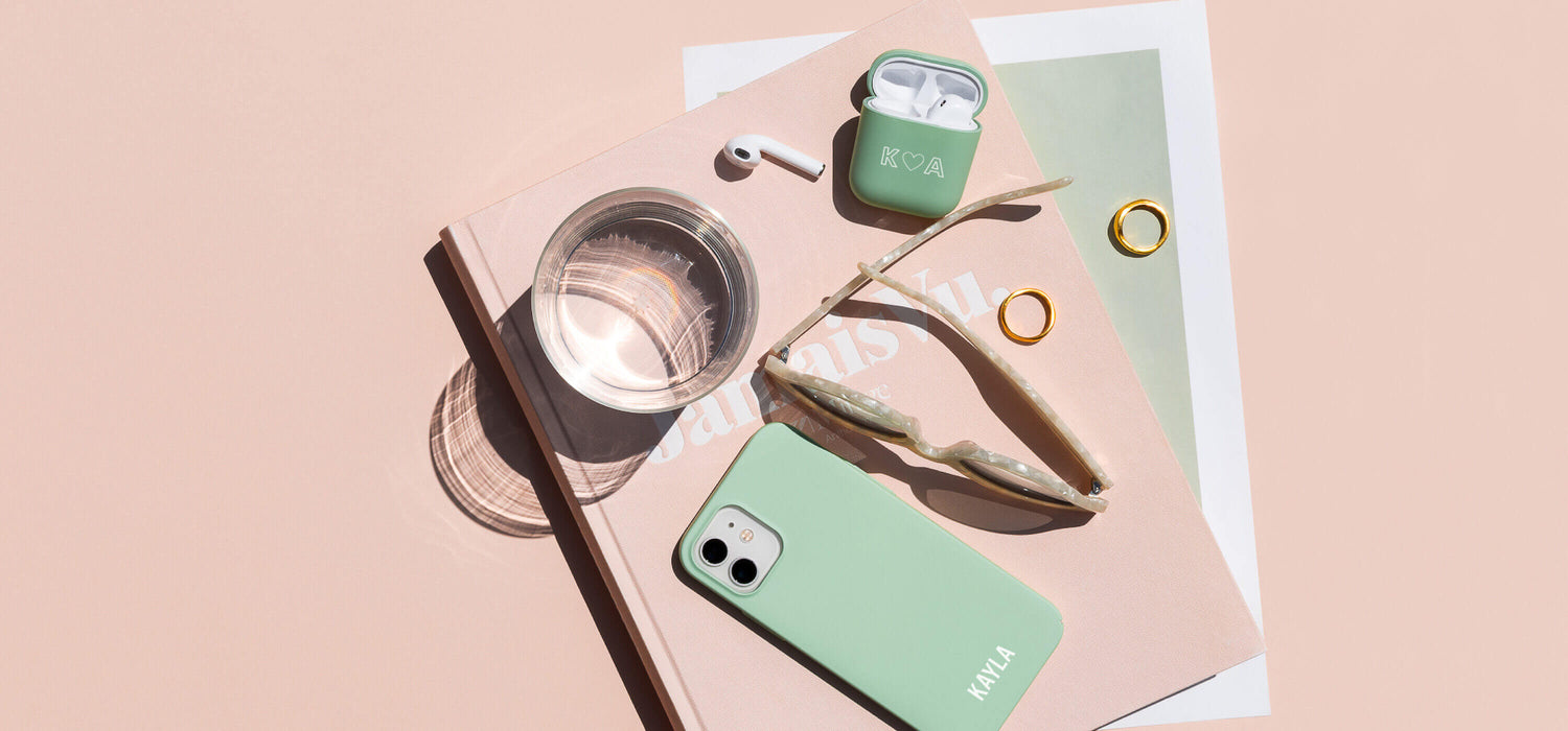 daily office essentials arranged on a desk with magazine, water, AirPods, phone and sunglasses