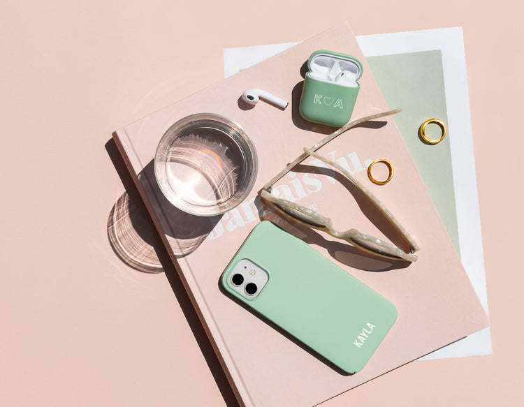 daily office essentials arranged on a desk with magazine, water, AirPods, phone and sunglasses