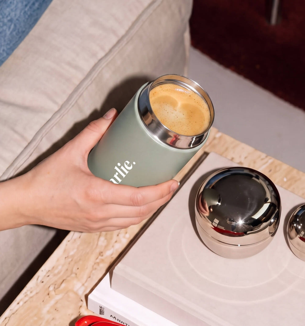 Beysis sage 340ml reusable coffee cup personalised with a name, lid off and filled with coffee beside a sofa