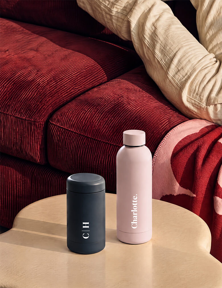 Beysis blush 500ml water bottle personalised with the name Charlotte beside a navy coffee cup with the initials C H