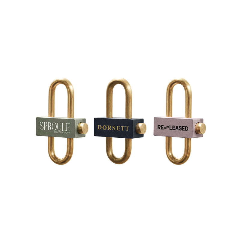 Beysis satin-finish brass keyrings in sage, navy and mauve, each branded with a different company logo