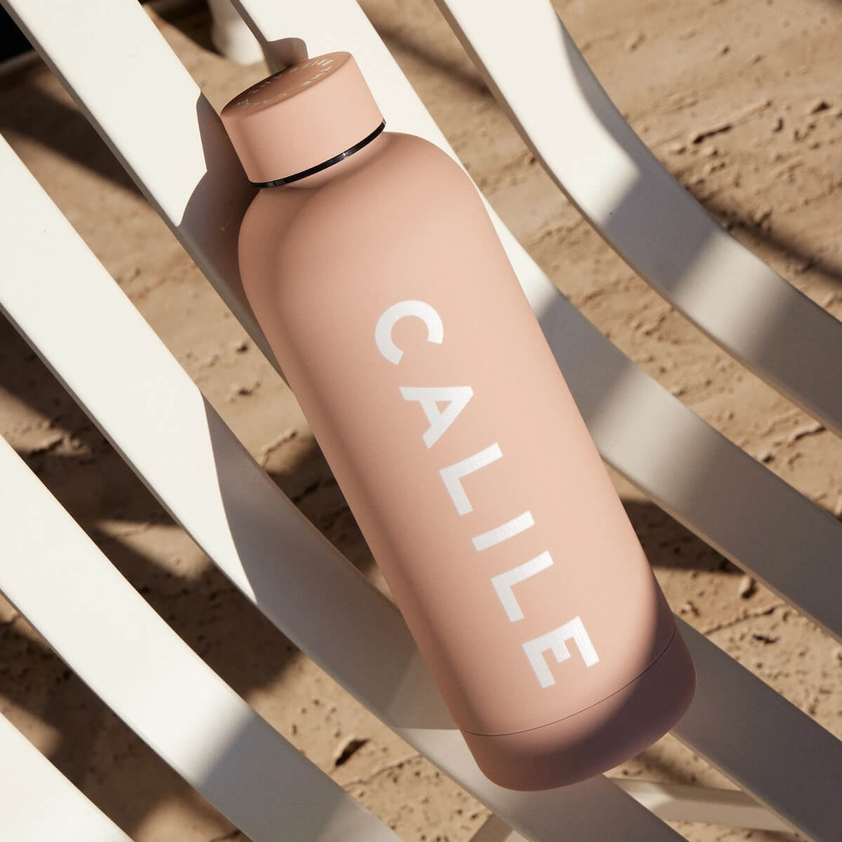 Beysis blush 500ml stainless steel water bottle branded with a company logo, resting on a white sun lounger