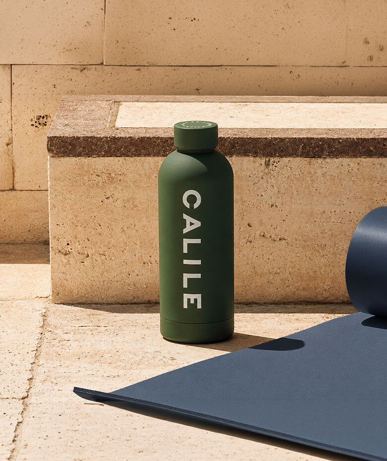 Beysis olive green 500ml stainless steel water bottle branded with a company logo, beside a yoga mat on sunlit stone